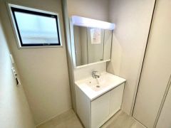 窓から自然光が差し込む明るい洗面室。収納豊富な三面鏡洗面化粧台を備え、使い勝手と機能性を兼ね備えた快適な空間です。